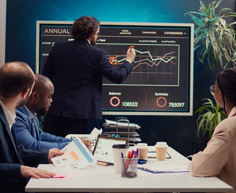 Investment team reviewing stock portfolio performance charts on a large screen during a meeting.