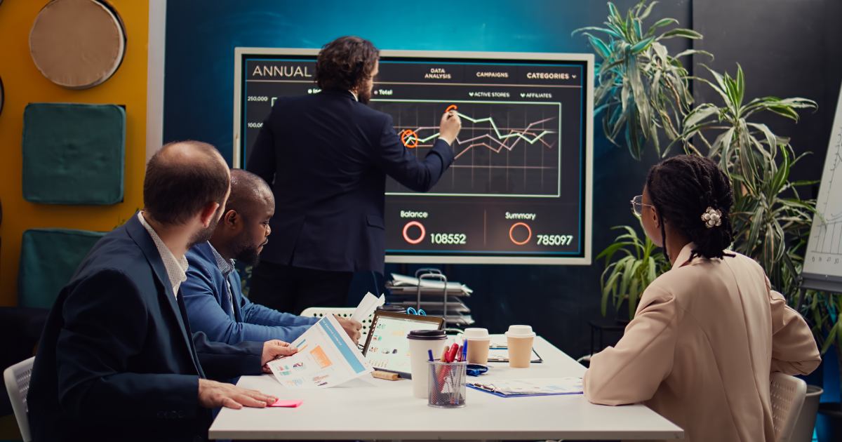 Investment team reviewing stock portfolio performance charts on a large screen during a meeting.